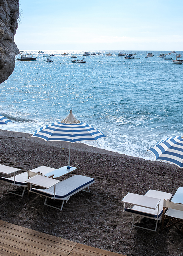 Relaxing beach day on the Amalfi Coast with striped umbrellas and calm waves moving softly A tranquil beach on the Amalfi Coast showcases lounge chairs under striped umbrellas, with gentle waves lapping at the shore and boats dotting the horizon, inviting serenity and relaxation.