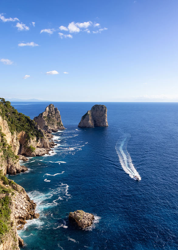 The Faraglioni rocks of Capri seen from the sea with a boat passing by.