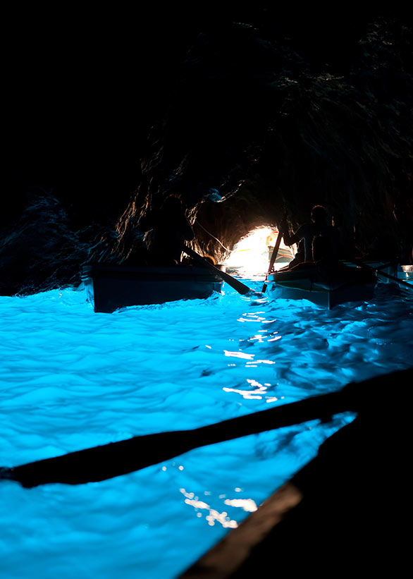 Boat inside the Blue Grotto of Capri with waters glowing in deep blue.